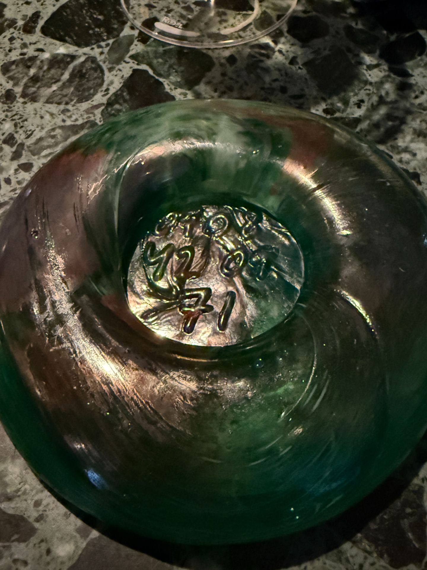 Close-up of a green glass piece with raised numbers in its centre on a veined stone table.