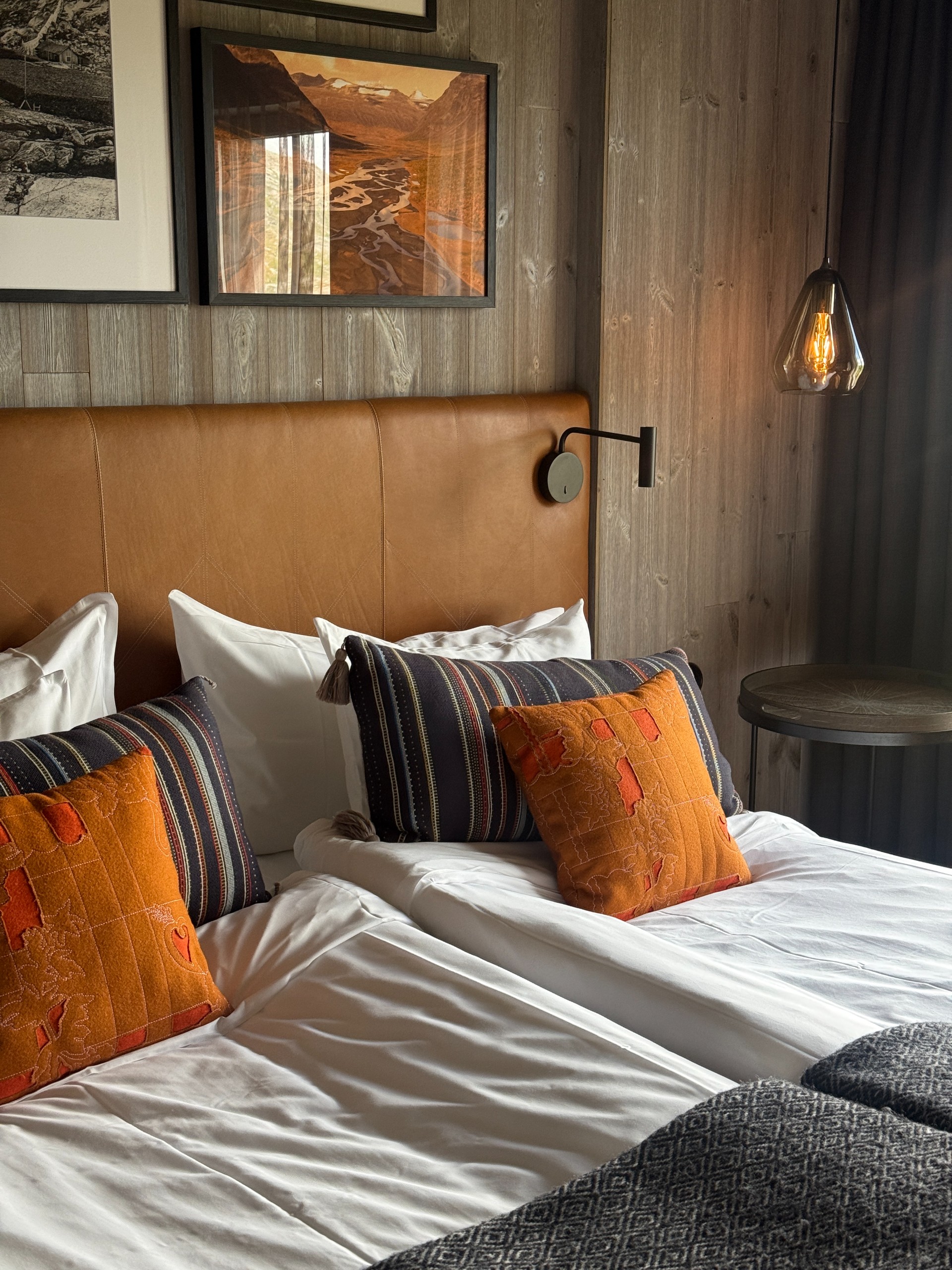 Twin beds with a tan leather headboard and patterned cushions in a timber-panelled guest room.