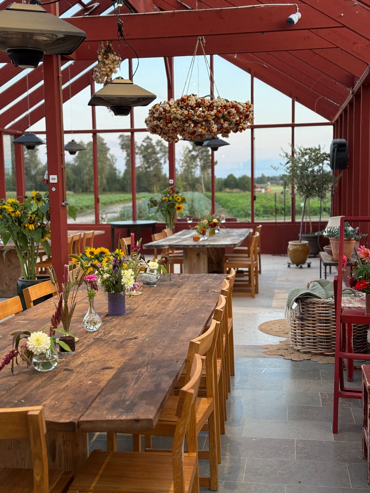 Flower-filled tables beneath red beams in the glass-walled orangery.