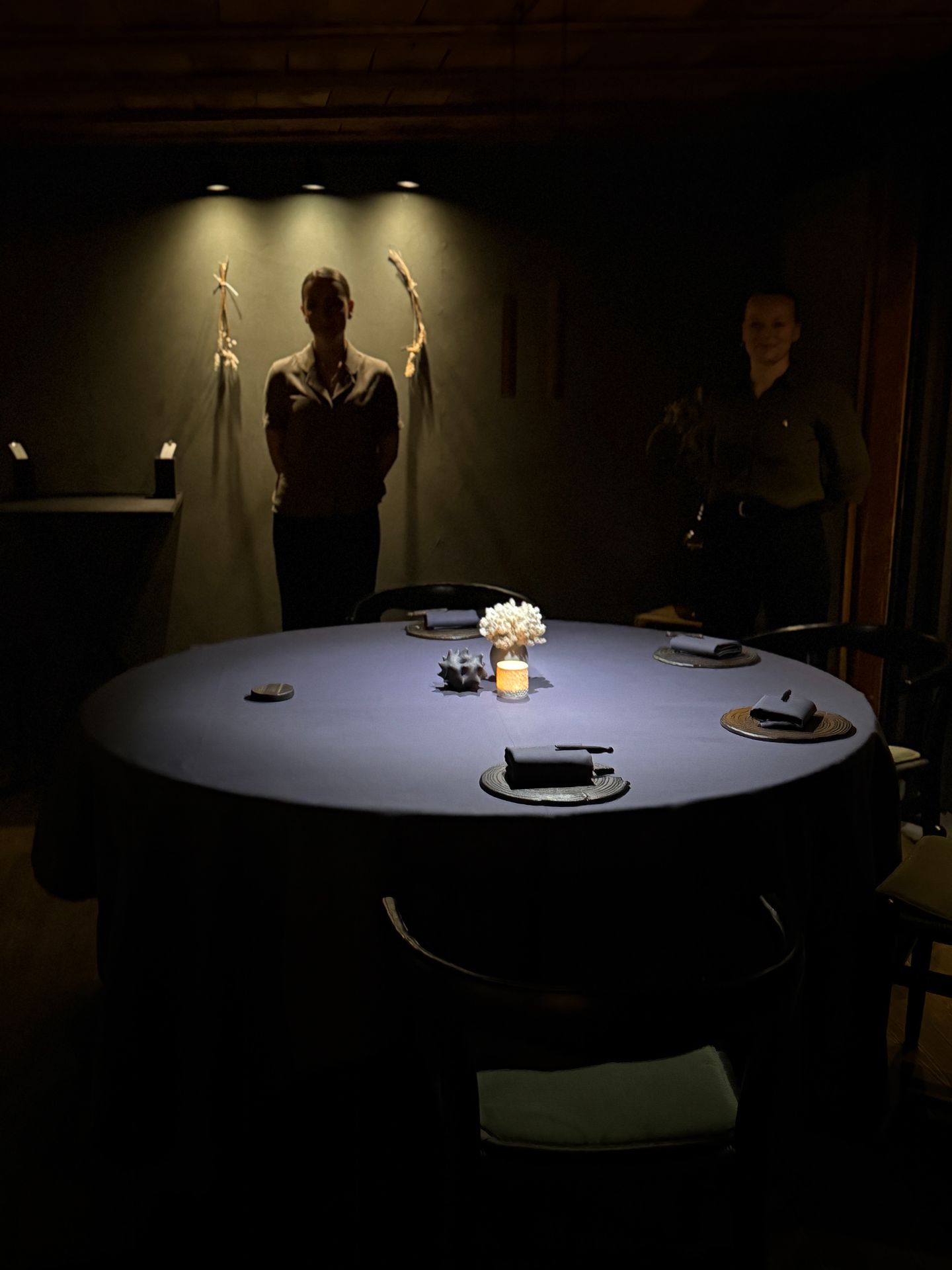 Two staff members standing behind a round table set with plates, folded napkins, flowers and a candle.