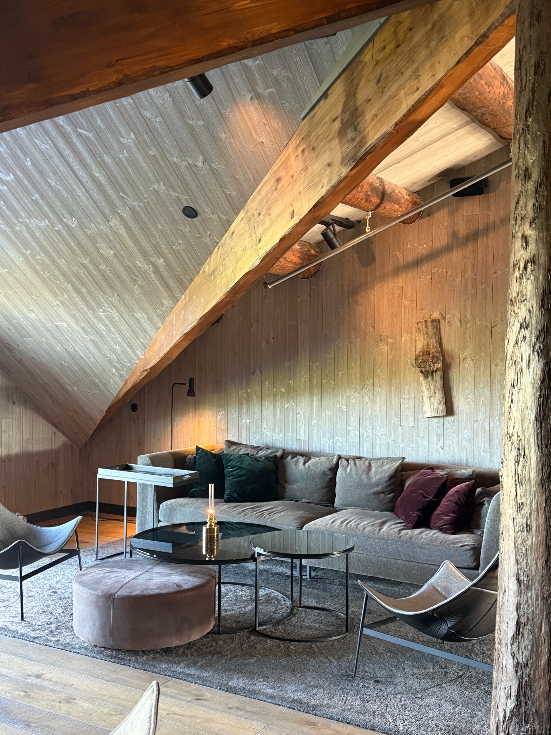 A grey sofa and lounge chairs beneath exposed timber beams.