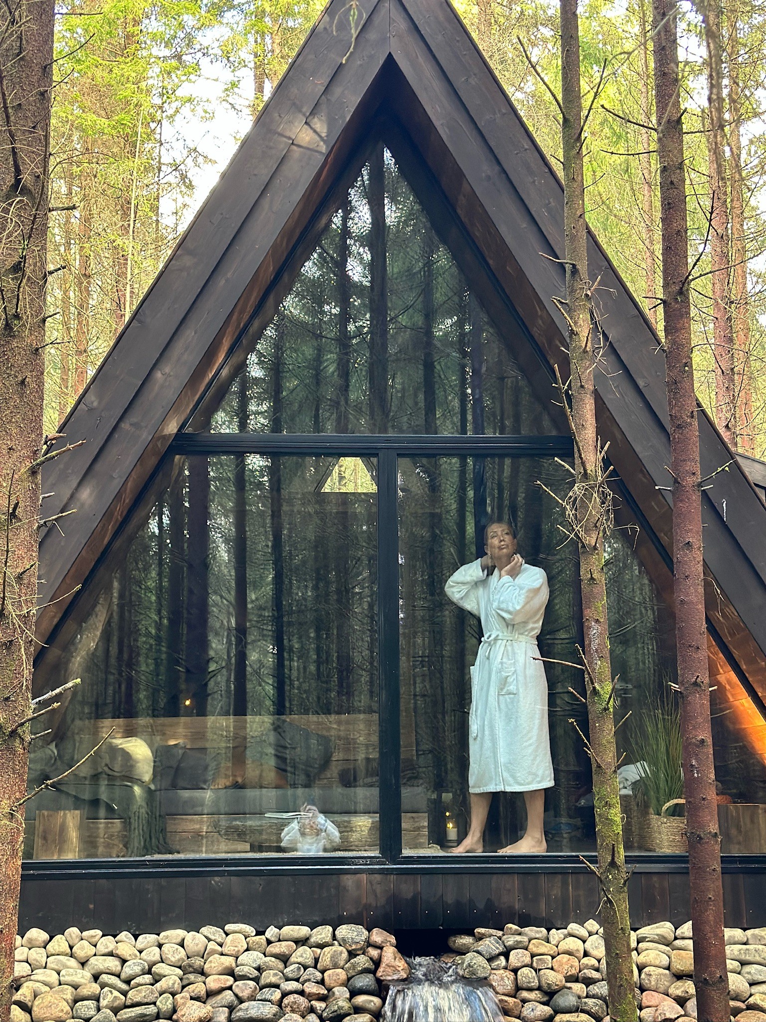 A guest in a bathrobe behind Creek Cabin’s triangular glass facade.