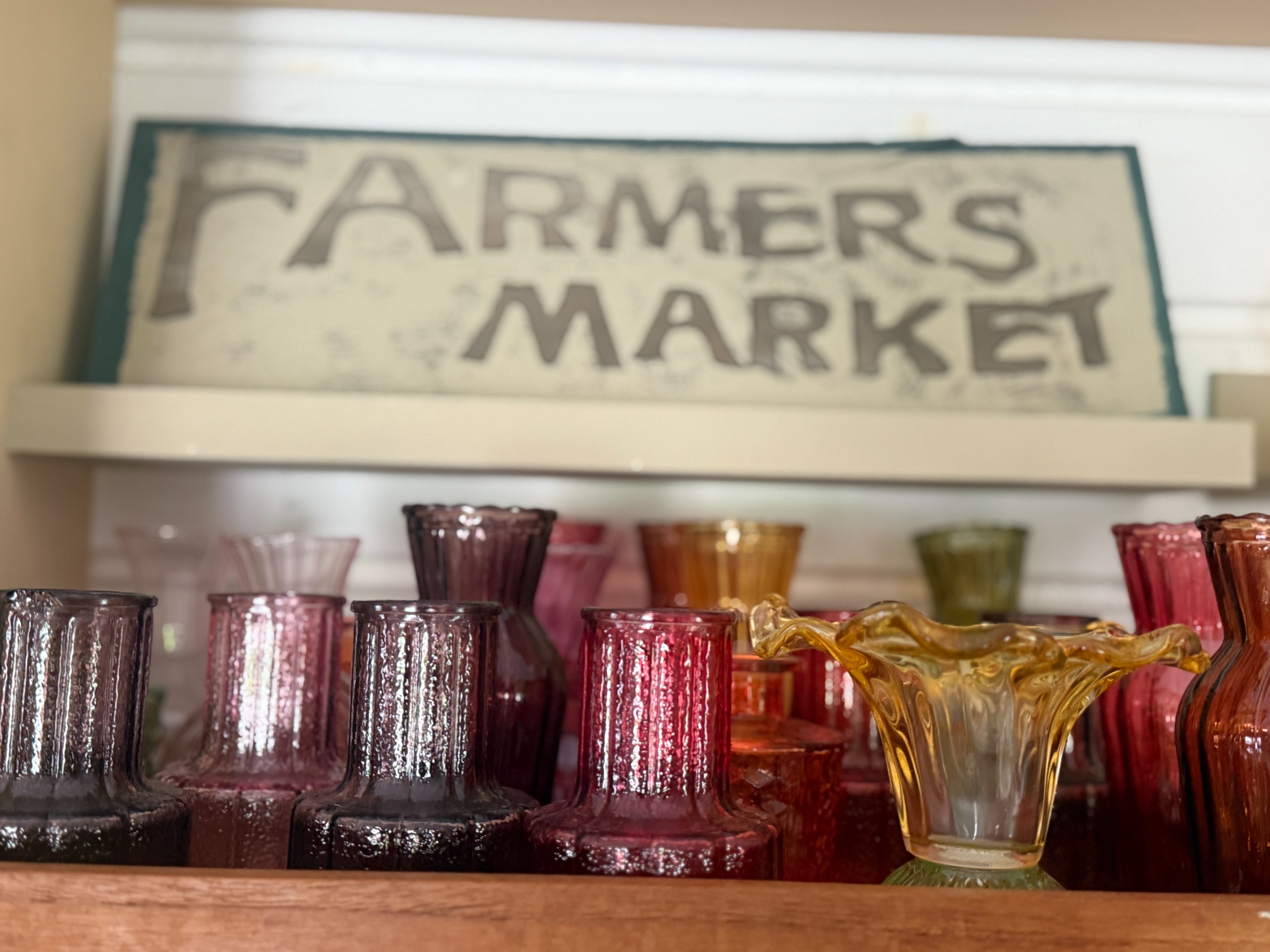 Colourful glass vases beneath a Farmers Market sign in the farm shop.