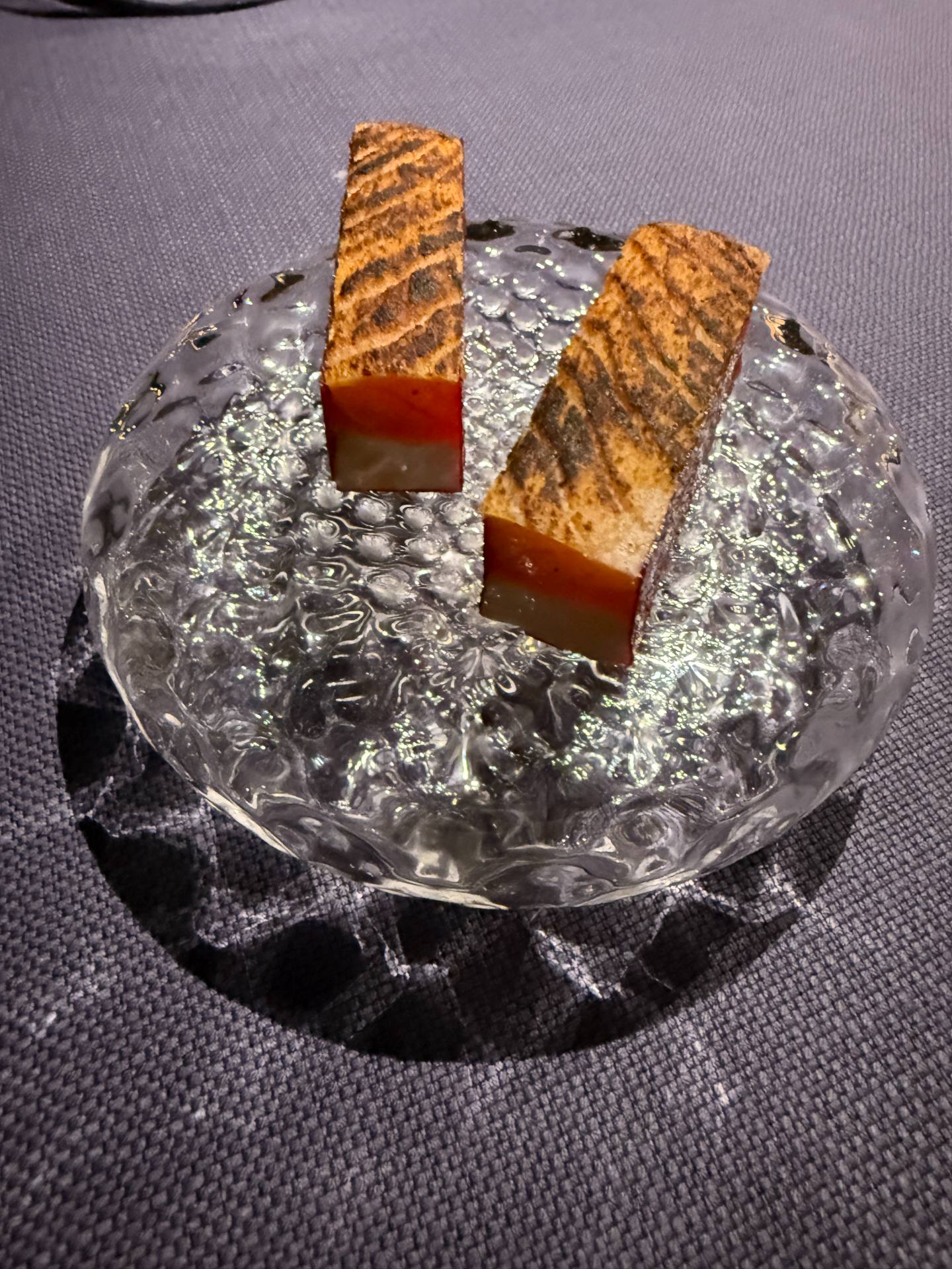 Two rectangular layered bites with browned tops on a textured clear glass plate.