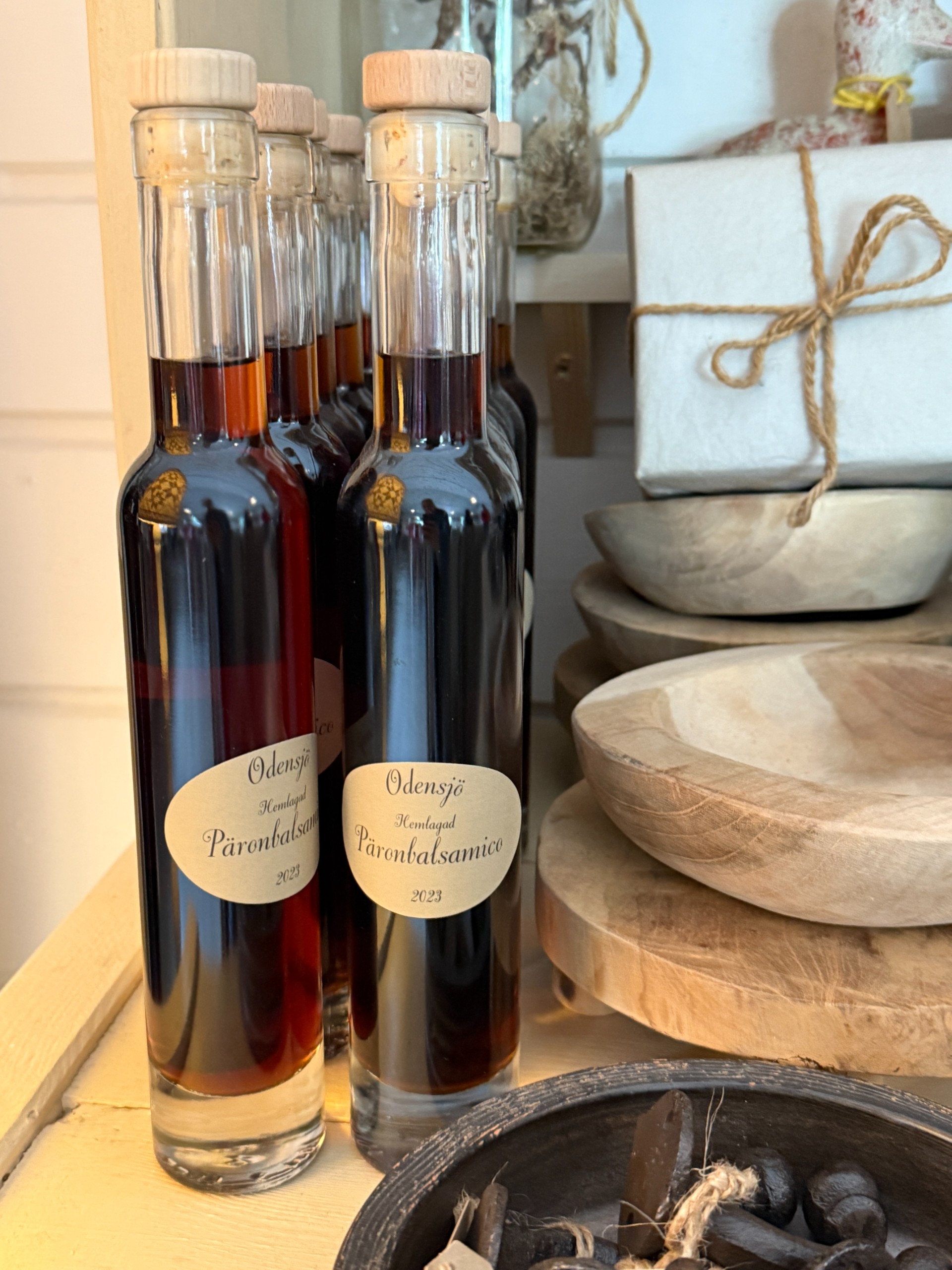 Bottles labelled Odensjö pear balsamic vinegar on a shop shelf beside wooden bowls.