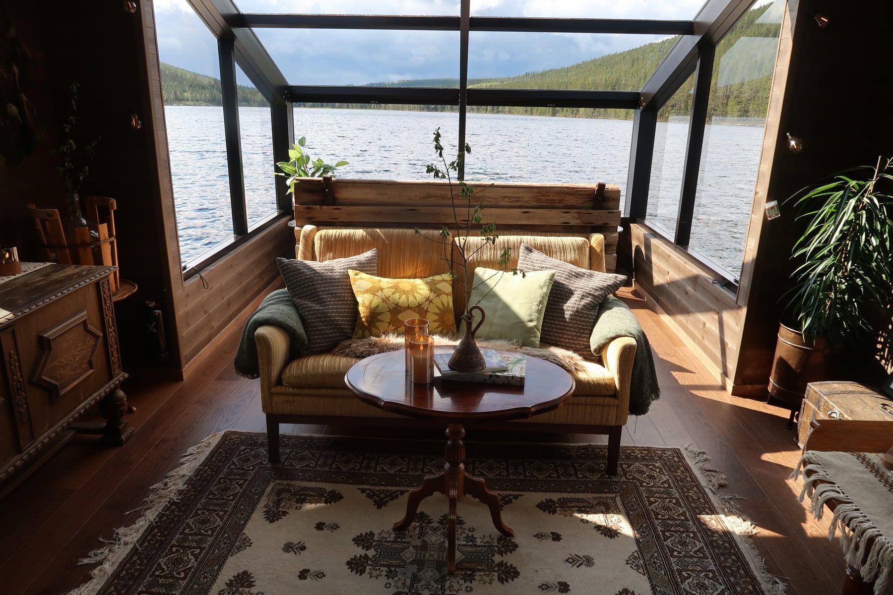 A yellow sofa and wooden furniture beneath the glass roof of Raven’s lake-facing room.