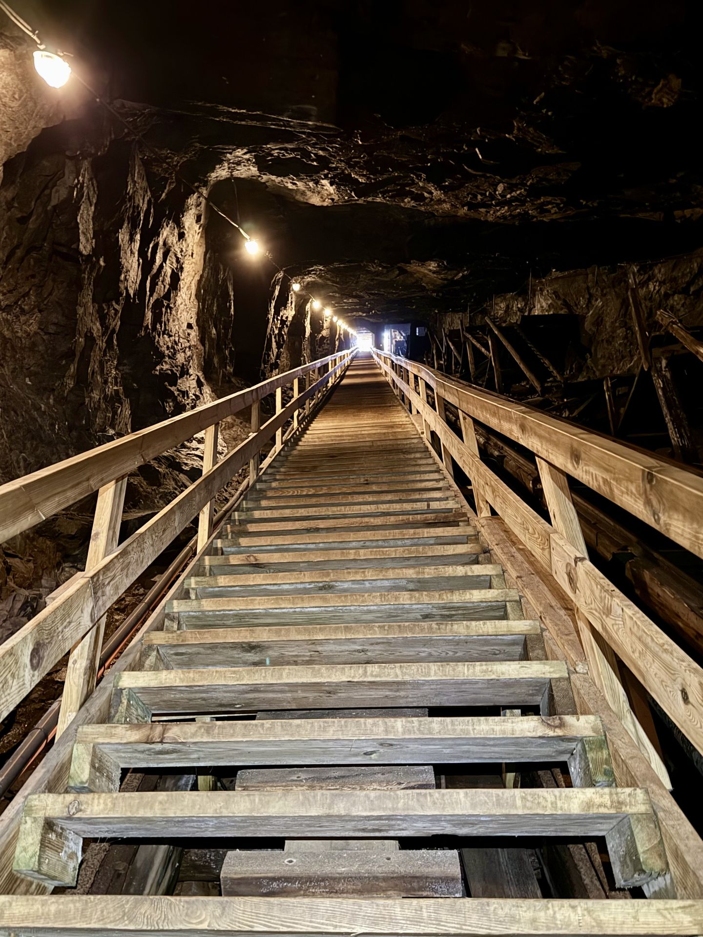 A long wooden staircase with handrails and electric lights runs through a rock shaft.