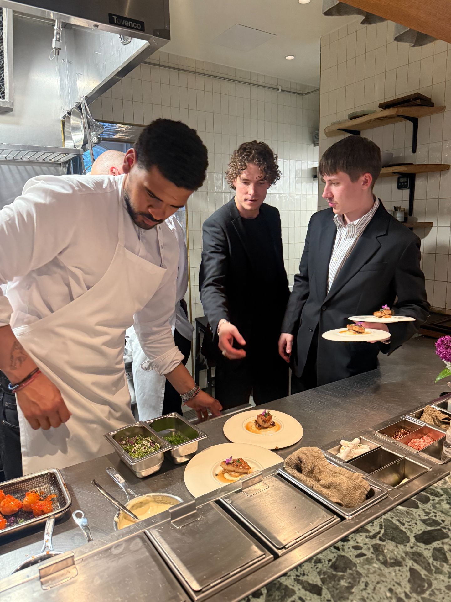 A chef finishing plates at Persona’s open kitchen counter as the service team collects dishes.