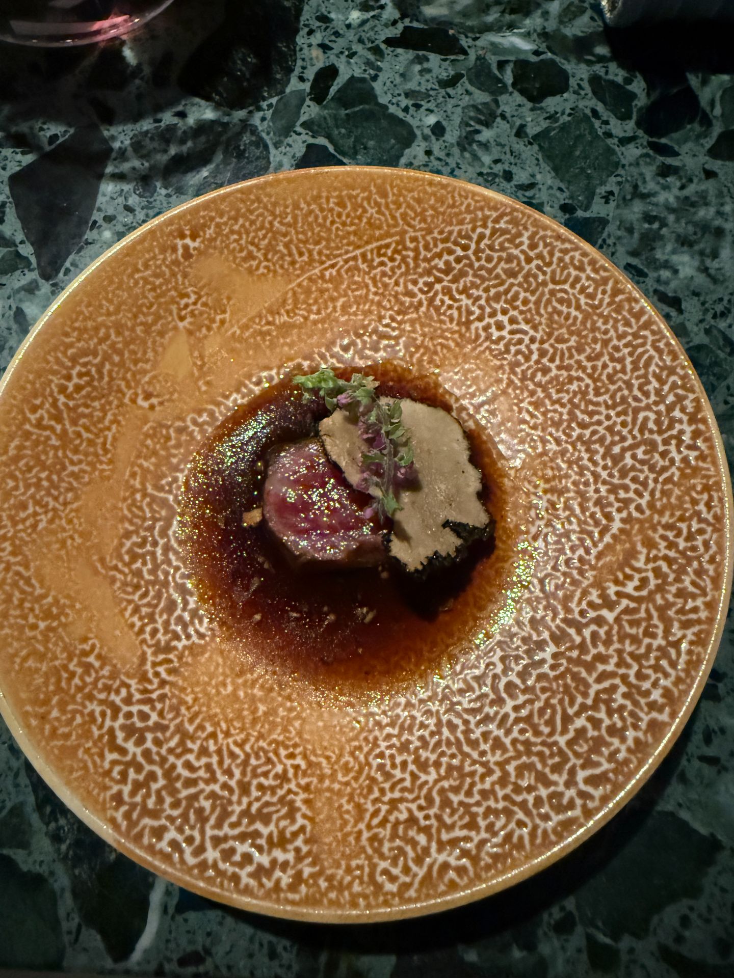 Wagyu topped with summer truffle in a dark sauce on a textured amber-coloured plate.