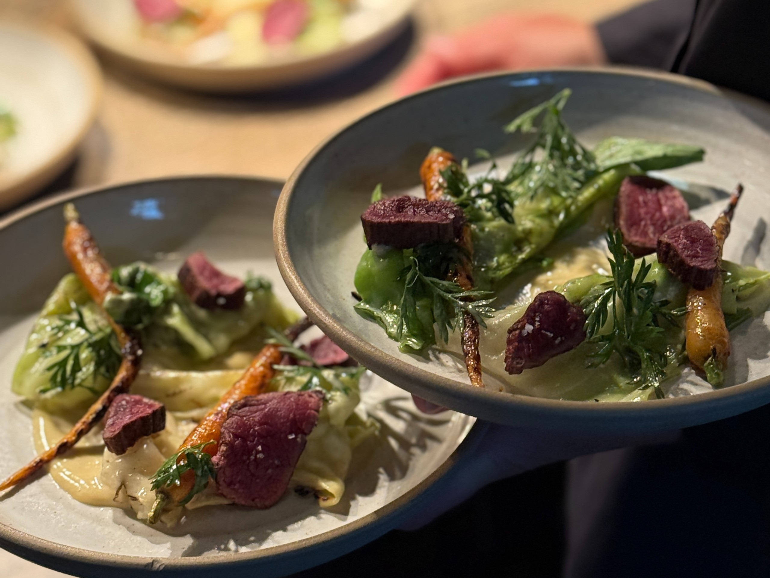 Plates of sliced meat with small carrots, greens and sauce.