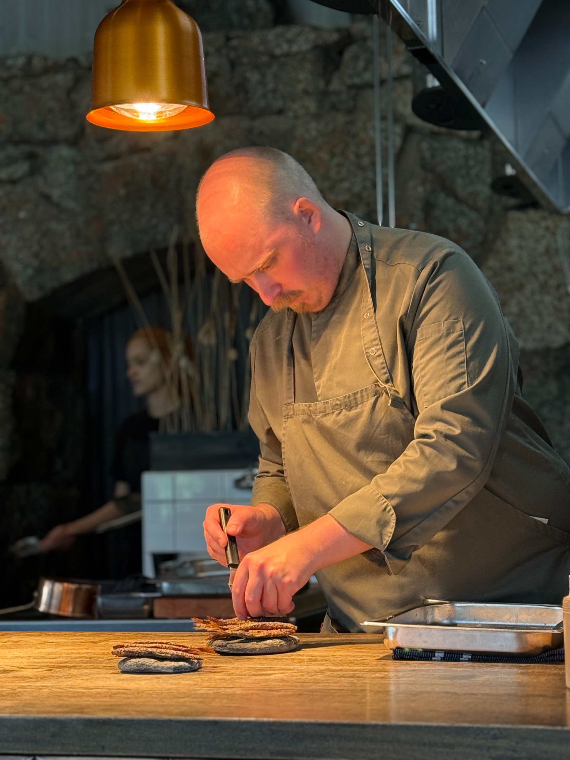 A chef arranges small fried fish on serving plates in the kitchen.